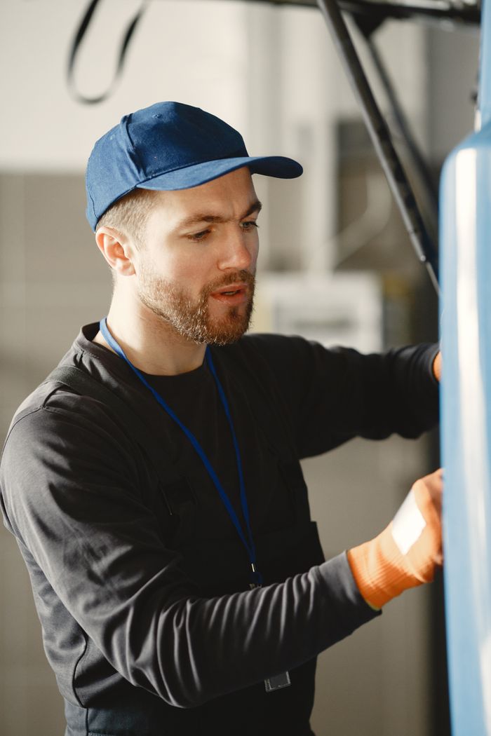 A male mechanic in a blue cap works on a vehicle indoors, focusing intently.